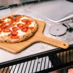 Paleta de bambú Ooni 16 con pizza de pepperoni en horno exterior