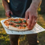 Paleta Pizza Ooni 12” Perforada sosteniendo pizza recién horneada.