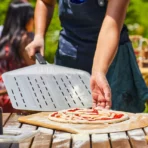 Paleta Pizza Ooni 12” Perforada deslizando pizza en el horno.